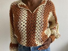 a woman wearing a brown and white crochet sweater standing in front of a wall