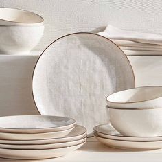 a stack of white dishes sitting on top of a table next to plates and bowls