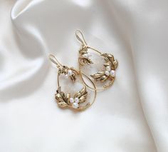 These handcrafted antique gold wedding earrings showcase a boho-inspired floral design, featuring delicate leaves and freshwater pearls. Expertly made to order, these hoop earrings add a touch of elegance and uniqueness to any bridal look. - Handcrafted in my PA studio - Genuine Austrian golden shadow crystal rock fabric leaves - Freshwater pearls - Antique gold leaves  - Available in rose gold, yellow gold or rhodium (silver) - Earrings measure 2.5 inches x 1-5/8 inch - Handcrafted in the US. - Nickel free and hypoallergenic - PLEASE ALLOW APPROX 10 BUSINESS DAYS FOR COMPLETION BEFORE SHIPPING. This is an original design by © Treasures by Agnes Browse our earrings: https://www.etsy.com/shop/treasures570?ref=seller-platform-mcnav&section_id=6861728 Browse our backdrop necklaces: https://ww Gold Earrings With Intricate Design For Wedding, Vintage Dangle Flower Earrings For Wedding, Gold Brass Hoop Earrings For Wedding, Delicate Brass Wedding Earrings, Yellow Gold Brass Earrings For Wedding, Brass Filigree Hoop Earrings For Wedding, Vintage Gold Pearl Earrings For Wedding, Elegant Brass Hoop Earrings For Wedding, Delicate Gold Hoop Earrings For Wedding