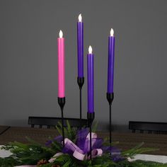 purple candles are lit on a table with greenery