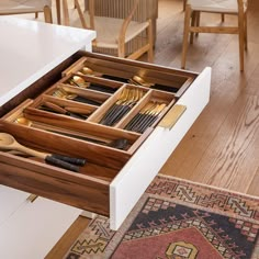 an open drawer with utensils and spoons in it on a wooden floor