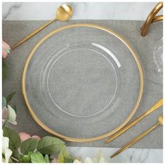 a place setting with gold rimmed plates and silverware on a gray linen napkin