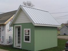 a small green house with a metal roof and white trim on the side of it