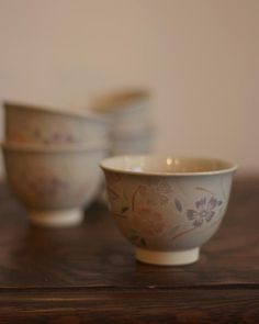 three bowls sitting on top of a wooden table next to each other with flowers painted on them