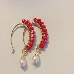 a pair of red and white beaded earrings with gold hooks on a white surface