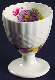 a white bowl with purple flowers painted on the outside and inside, sitting on a pedestal