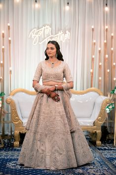 a woman standing in front of a white couch wearing a dress and holding her hands together