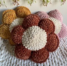 several crocheted flowers sitting on top of a white blanket next to a plant