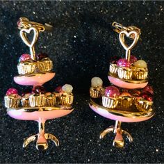 pair of pink and gold earrings with hearts on each earring, sitting on a black surface