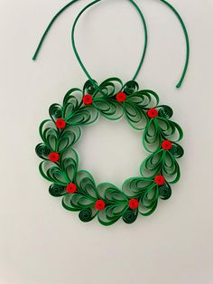 an origami wreath with red flowers and green string hanging from it on a white surface