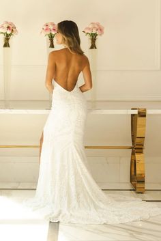 a woman in a white wedding dress is standing by a bench with flowers on it