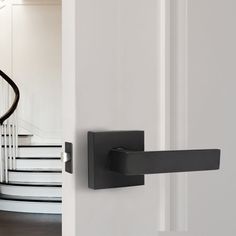 an open door with a black handle next to a white stair case in a house