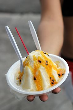 a person holding a paper plate with ice cream and strawberries