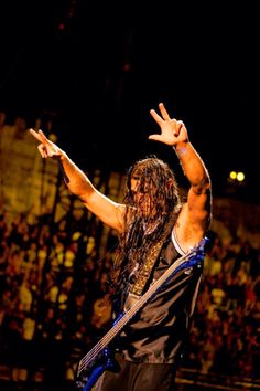 a man with long hair holding his arms up in the air while standing on stage