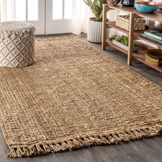 a large rug with fringes on the floor in front of a wooden table and bookshelf