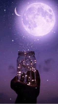 a person holding up a jar with lights in it and the moon above them at night