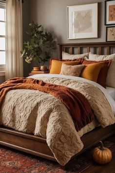 a bed with orange and brown comforters in a bedroom next to a window, pumpkins on the floor