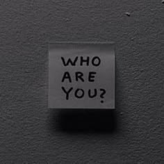 a sign that says who are you? on a black surface with small dots around it