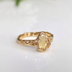 a gold ring with an oval shaped yellow diamond in the center on a white surface