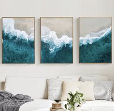 three paintings hang on the wall above a white couch in a living room with a coffee table