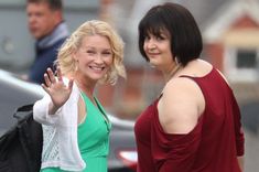 two women standing next to each other waving