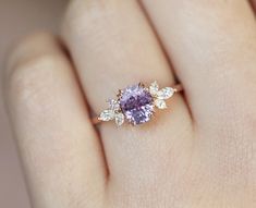 a woman's hand holding a ring with a purple stone and white diamonds on it