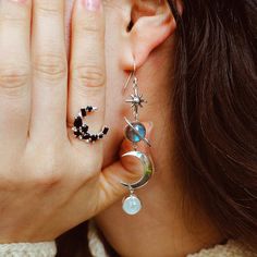 Stunning and sparkly celestial dangly earrings for boho women. These sterling silver earrings feature labradorite and Moonstone gemstones with celestial imagery including a star, planet Saturn and a crescent moon. Labradorite is commonly known as the stone of things ‘unseen.’ It provides energetic and spiritual protection while also warding off negative vibes. Moonstone delicately connects us to the wisdom of the moon and our own inner goddess. It is also deeply connected to water. Material: Gen Celestial Sterling Silver Earrings, Silver Celestial Gemstone Earrings, Celestial Moonstone Jewelry With Sun And Moon Design, Celestial Sun And Moon Moonstone Jewelry, Celestial Silver Pierced Crystal Earrings, Celestial Silver Moonstone Earrings, Silver Moon-shaped Celestial Earrings, Silver Moon Shaped Celestial Crystal Earrings, Celestial Moon Phase Earrings