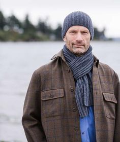 a man standing in front of a body of water wearing a gray hat and scarf