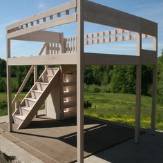 a wooden structure with stairs on the top and bottom floor, in front of a grassy field