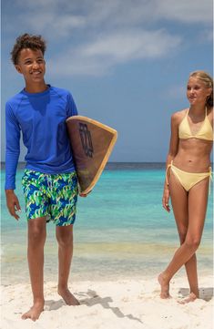 two young people standing on the beach holding surfboards in their hands and smiling at the camera