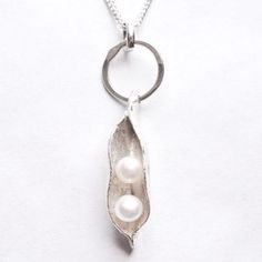 a silver necklace with two pearls hanging from it's center, on a white background