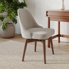 a beige chair sitting on top of a rug next to a table and potted plant