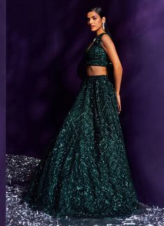 Introducing the exquisite Emerald Green Sequins Embroidered Lehenga Set, a masterpiece of elegance and sophistication. Crafted from delicate net fabric, this flowing green lehenga is meticulously adorned with tonal multi-cut sequins, crystals, and bugle beads, creating a mesmerizing shimmer that captivates with every movement. The intricate embroidery adds depth and richness, enhancing the luxurious appeal of the ensemble. Paired with a matching V-neckline blouse that perfectly balances the modern and traditional elements. Completed with an embellished dupatta for a cohesive, stunning look. Ideal for the bride or bride-to-be, especially for Cocktail or Sangeet nights, this lehenga set ensures you will be the center of attention, radiating timeless allure and unmatched opulence. Composition Green Embellished Anarkali Choli, Anarkali Embellished Green Choli, Anarkali Style Embellished Green Choli, Green Organza Lehenga With Sequins, Green Organza Gown For Designer Wear, Embellished Green Floor-length Choli, Embellished Green Anarkali Set For Party, Embellished Green Lehenga For Festive Occasions, Green Embellished Anarkali Set For Party