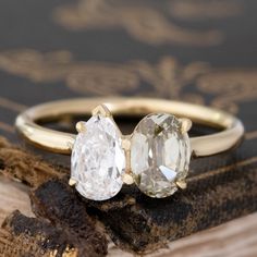 two engagement rings sitting on top of a piece of wood next to an old book