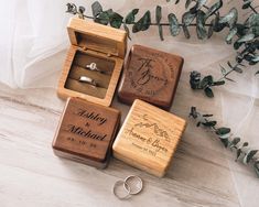 three wooden ring boxes with wedding rings in them on a table next to greenery