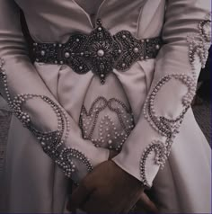 a woman in a white dress with pearls on her hands and an elaborate belt around her waist