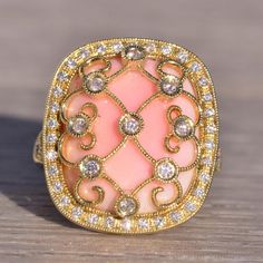 The 154th Avenue: Pink Coral And Natural Diamond Cocktail Ring In Yellow Gold. The Ring's Focal Point Is A Central Round-Cut Natural Diamond Ensconced Within A Lattice Of Yellow Gold Lace Adorned With Natural Diamonds. Below This Intricate Design Rests A Cushion Buff Top Made Of Exquisite Pink Coral. Encircling The Coral Is A Halo Of Round-Cut Natural Diamonds. The Split Shank Of The Ring Is Also Adorned With Round Brilliant-Cut Natural Diamonds. Delicate Milgrain Detailing Graces The Lacework, Both Outside The Halo And Around The Bezels. Crafted In 14 Karat Yellow Gold, The Ring Is Currently Sized At 6.75 But Can Be Resized To Fit Any Finger Size For An Additional Charge Upon Request. Luxury Pink Diamond Ring For Formal Occasions, Luxury Pink Diamond Gemstone Ring, Luxury Pink Jewelry With Prong Setting, Exquisite Pink Rings With Diamond Accents, Luxury Pink Diamond Ring For Anniversary, Luxury Pink Rings With Pave Setting, Pink Diamond Ring With Pave Setting For Gift, Pink Diamond Ring With Pave Setting As Gift, Exquisite Pink Diamond Ring With Accents