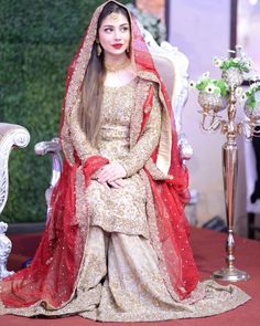 a woman sitting on top of a chair wearing a red and gold dress with a veil