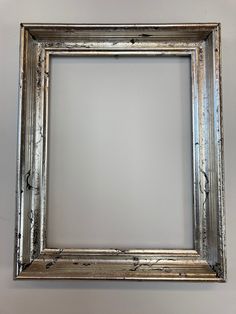 an old silver frame hanging on the wall with white paint and peeling paint all over it