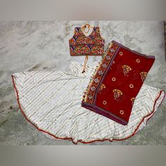 Designer Latest Fashion Chaniya Choli, Perfect For Navratri Or Any Other Occasion! Colorful Choli With Traditional Gamthi Work, Along With Gamthi Mirror Work Dupatta. Vibrant Color Paired With White Golden Chaniya. Blouse Measurements - Chest 40” Can Extend Upto 42” (Adjustable With Strings To Tie In The Back) - Waist 38” - Length 16” Chaniya Measurements - Length 39” - Waist 40” - Hip 60” White Bohemian Traditional Wear For Ceremonies, Bohemian White Traditional Wear For Ceremonies, White Sharara With Zari Work For Festivals, Traditional White Sharara For Festivals, Fitted White Sharara For Navratri, Red Choli With Traditional Patterns For Puja, White Sharara With Zari Work For Navratri, Red Sets With Gota Work For Puja, White Anarkali Style Choli For Navratri