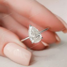 a woman's hand holding an engagement ring with a pear shaped diamond