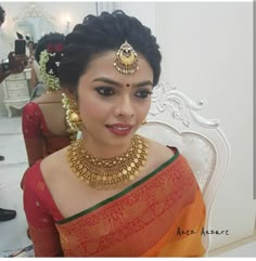 a woman in an orange and green sari with gold jewelry on her neck, sitting down