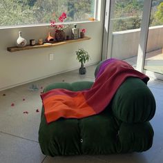 a green bean bag chair covered in a red and orange blanket next to a window