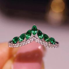 someone is holding a ring with emeralds and diamonds on it