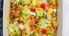 a casserole dish with cheese, lettuce, tomatoes and other toppings