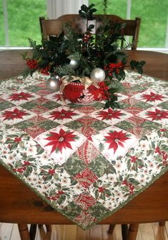 a christmas table cloth with poinsettis and greenery on it, in front of a window