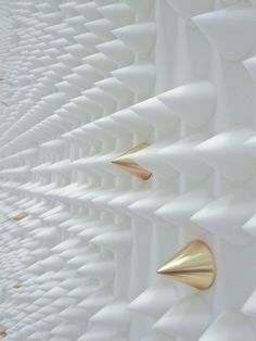 an abstract white and gold sculpture with three brass spikes on it's sides, against a white background