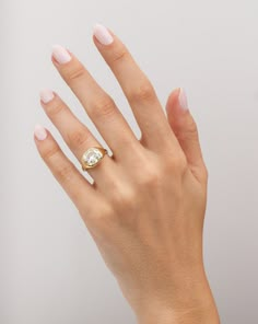 a woman's hand wearing a gold ring with a white diamond on the middle