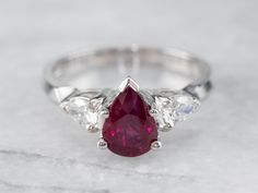 Always in style, rings such as this one can be worn as engagement rings, thanks to their high quality and the secure style of this setting. We've set the center of this one with a pretty, glowing red ruby cut into a romantic teardrop shape. The bright white diamonds reflect plenty of light into the deep, luscious red center stone. This ring will look well with a variety of bands, from a plain circle to a ruby and diamond eternity band. Metal: 18K White Gold Gem: Ruby 1.03 Carat Gem Measurements: Luxury Silver Ruby Ring With Rose Cut Diamonds, Luxury Ruby Ring With Single Cut Diamonds, Luxury Ruby Ring With Tension Setting, Luxury Ruby Diamond Ring With Prong Setting, Luxury Elegant Ruby Ring With Tension Setting, Luxury Ruby Ring With Tension Setting As Gift, Luxury Elegant Ruby Ring With Prong Setting, Luxury White Gold Ruby Ring With Rose Cut Diamonds, Luxury Ruby Ring With Tension Setting For Wedding