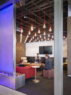 two people are sitting at a table in an office with red and blue lights hanging from the ceiling